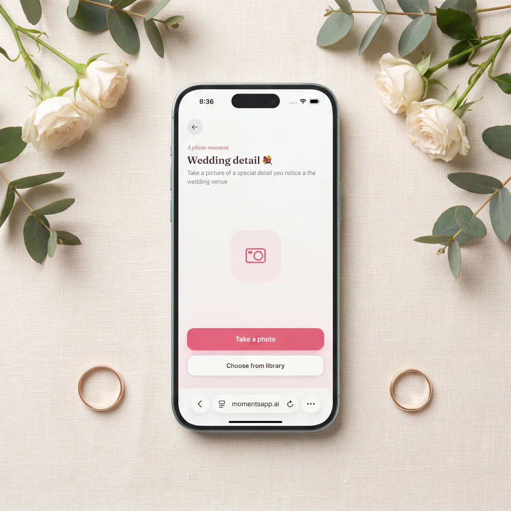 A phone among roses, eucalyptus, and two wedding bands, showing the “Wedding detail” photo prompt with options to take a photo or choose one from the library.